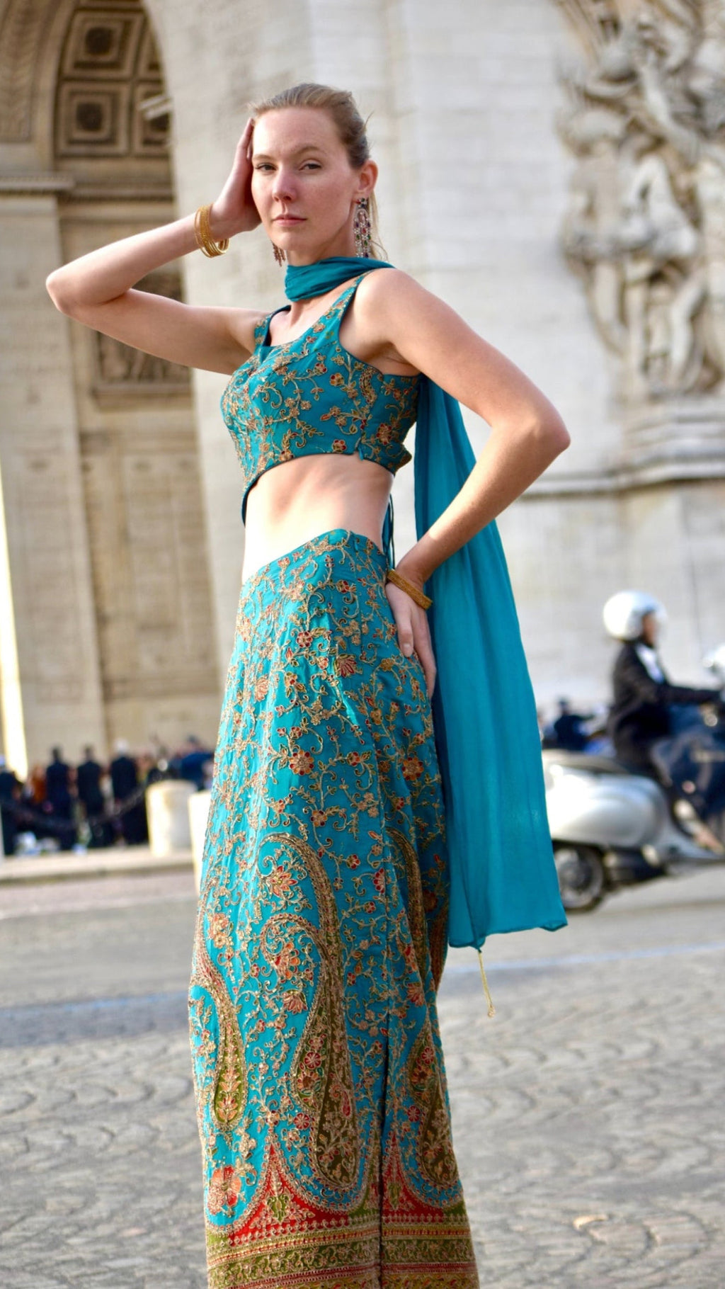 Woman in a teal and gold patterned outfit standing in front of a classical building.